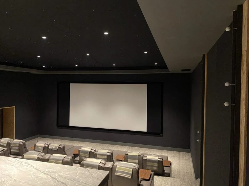 Finished home theater with dark painted walls, projection screen, and tiered seating